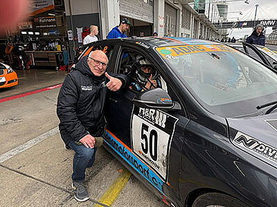 Darian Donkel sitzt im Rennwagen mit der Startnummer 50. Neben dem Auto kniet Jörg Hennig, Vorstand Sport des ADAC Mittelrhein und wünscht ihm Glück.